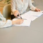 two people that are signing a document, a legal agreement that represents the relationship between a law firms or solicitors with their clients.
